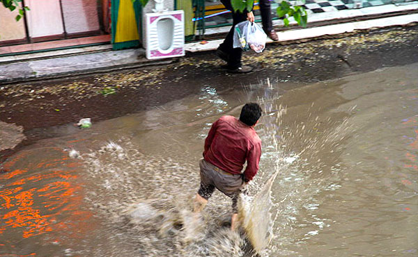 تلاش یکی از شهروندان اردبیل برای عبور از معبر آب گرفته در باران. (مهر)